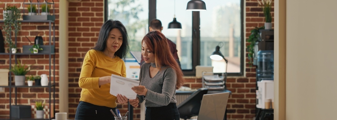 Zwei Frauen halten ein Blatt Papier in der Hand und sprechen miteinander.