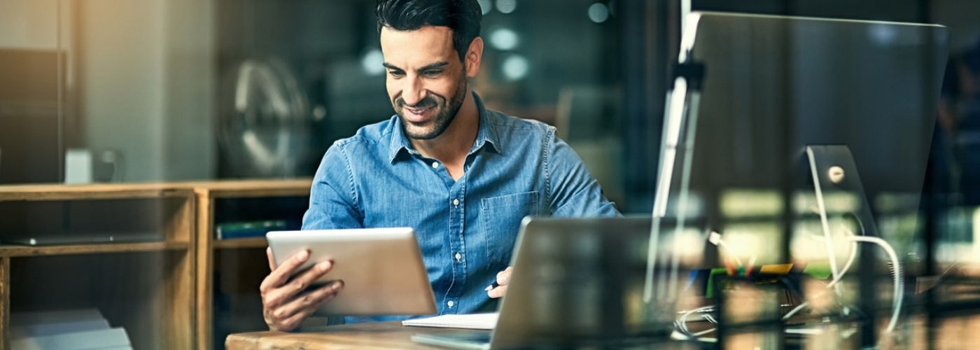 Ein Mann sitzt an einem Tisch und schaut auf ein Tablet.