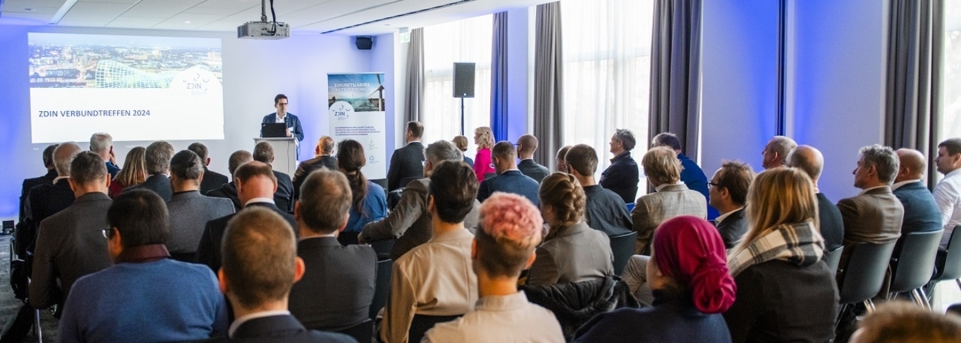 Ein Veranstaltungsraum voller Menschen, vorne hält ein Mann eine Präsentation.
