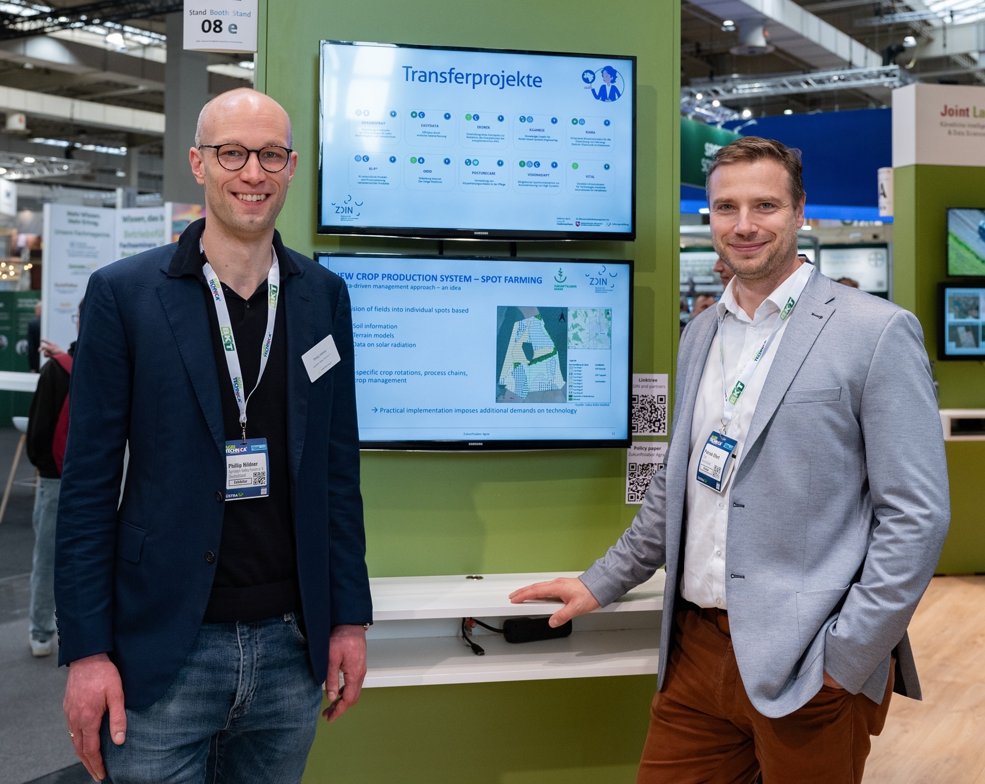 Zwei Männer stehen vor einer Stele und schauen in die Kamera.