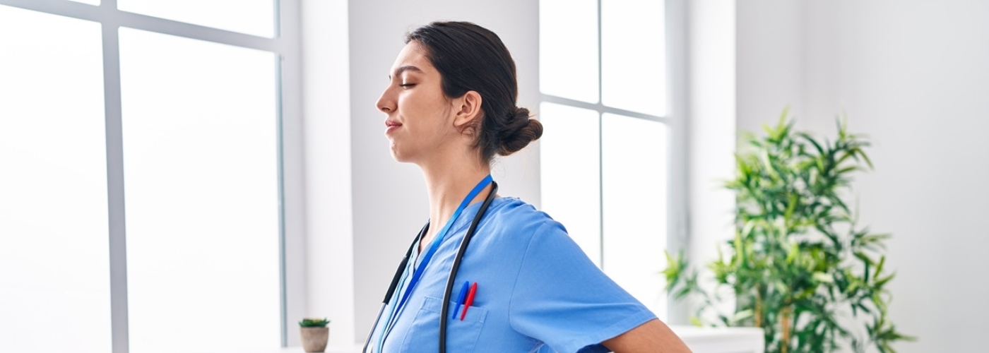 Eine Frau im blauen Kittel hält sich vor Schmerz den Rücken