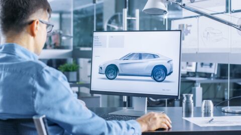 Ein Mann sitzt vor einem Monitor, auf dem ein Fahrzeugmodell zu sehen ist.