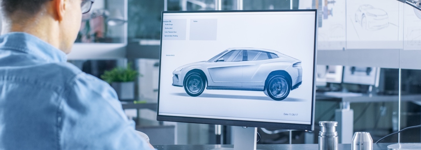 Ein Mann sitzt vor einem Monitor, auf dem ein Fahrzeugmodell zu sehen ist.