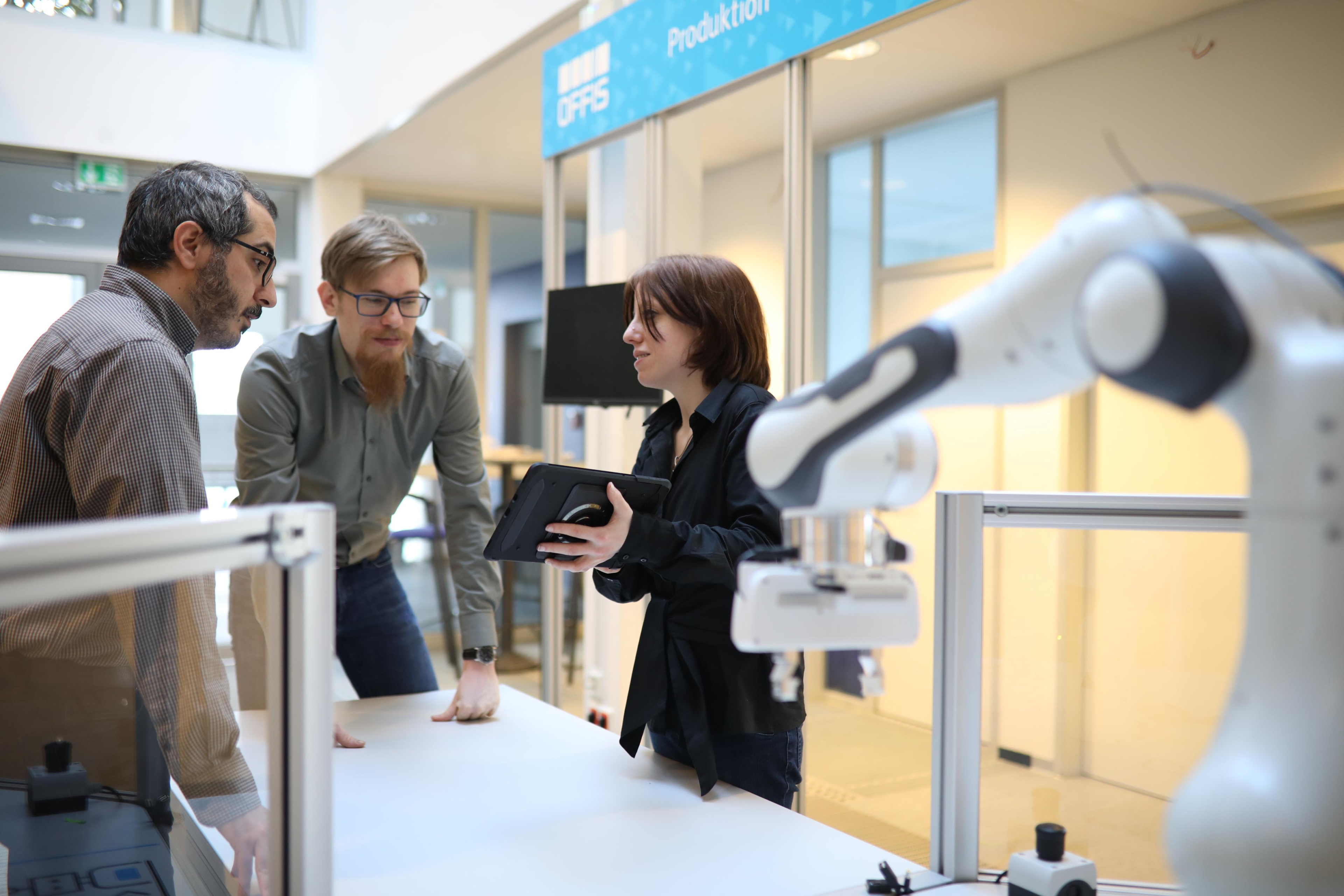 Drei Personen neben einem Roboterarm