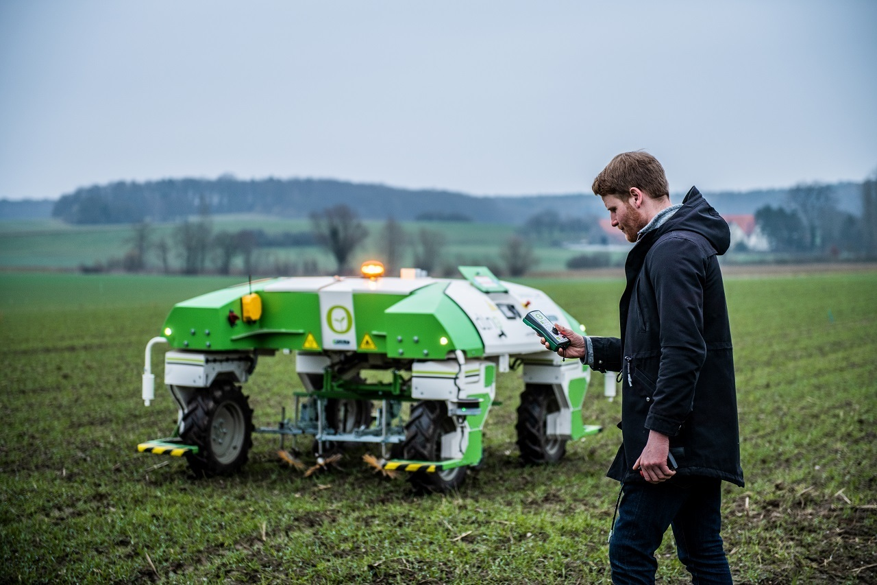 Eine Person steht neben einem Agrarroboter auf einem Feld