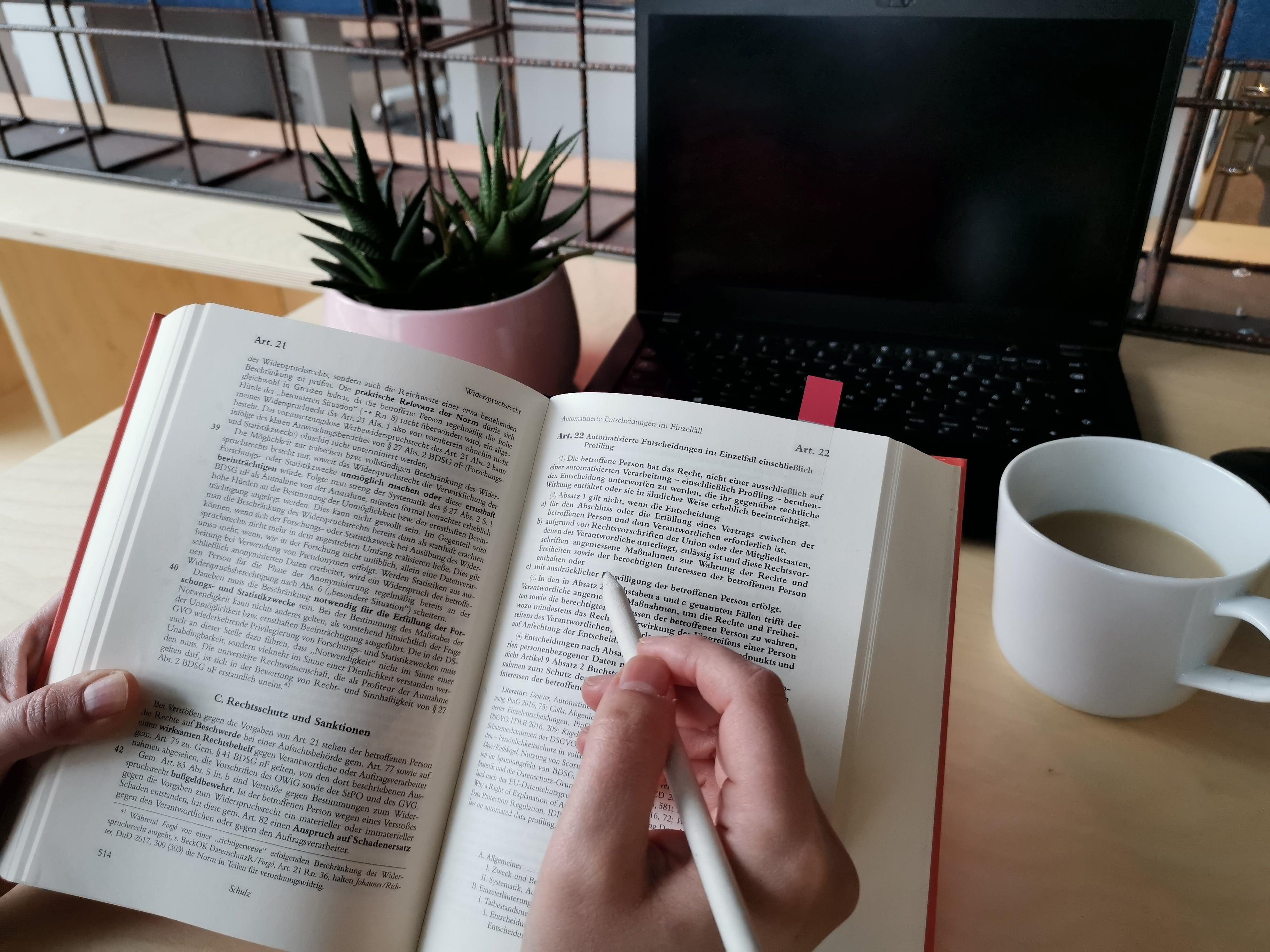 Person ließt ein Buch und hält einen Stift in der Hand