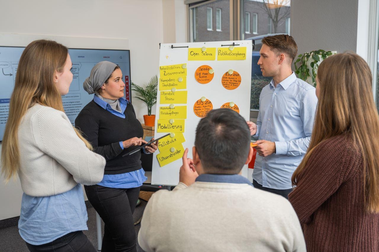 Mehrere Personen stehen vor einer Flipchart und besprechen etwas