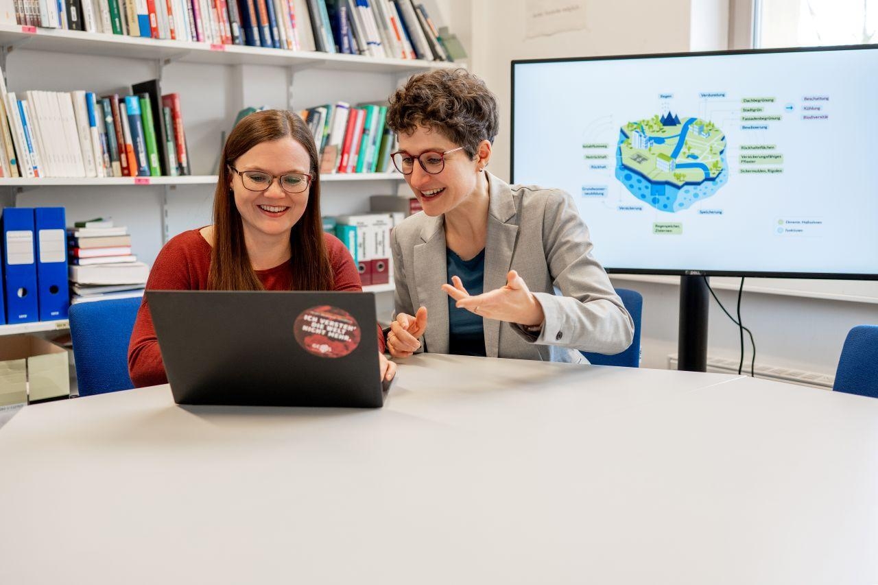 Zwei Frauen sitzen an einem Tisch vor einem Laptop.