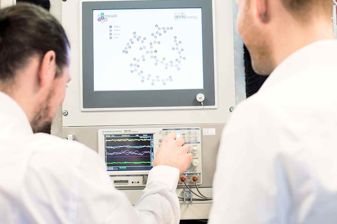 Zwei Personen stehen vor einem technischen Gerät mit Daten auf einem Bildschirm