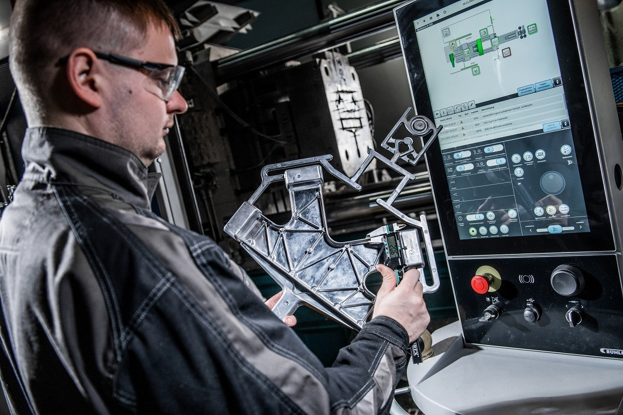 Mann steht vor Maschine und hält Metallgegenstand in der Hand