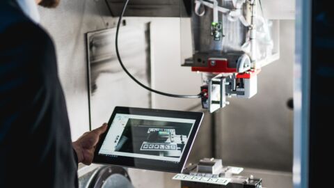 Mann steht mit Tablet vor einer Maschine