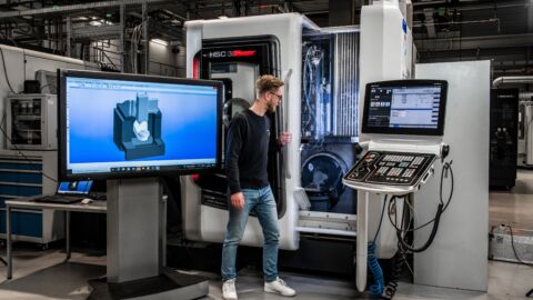 Eine Person steht vor einer großen Maschine mit Monitor