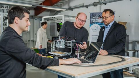 Mehrere Personen stehen an einem Tisch mit einem technischen Objekt darauf
