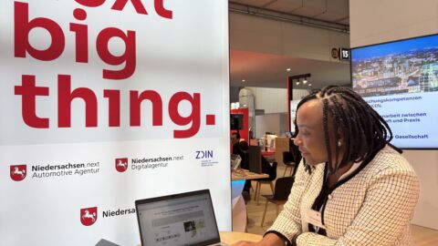 Eine Frau präsentiert an einem Messestand etwas auf einem Laptop.