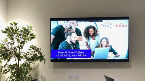 Ein Konferenzraum mit Fernseher auf dem eine Einladung zum Meet & Greet ist