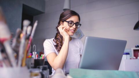Frau sitzt vor einem Laptop. Vor ihr stehen Pinsel