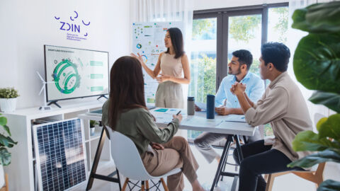 Eine Frau steht präsentiert eine Grafik des Zukunftslabors Circular Economy drei weiteren Personen, die an einem Tisch sitzen.