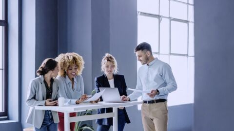 Vier Personen stehen an einem Tisch mit Laptops