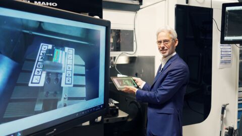 Mann steht vor einem Bildschirm und hält ein Tablet in der Hand