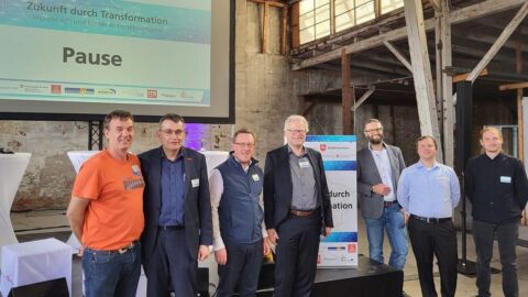 Eine Personengruppe steht vor einer Leinwand auf die "Pause" projiziert wird.