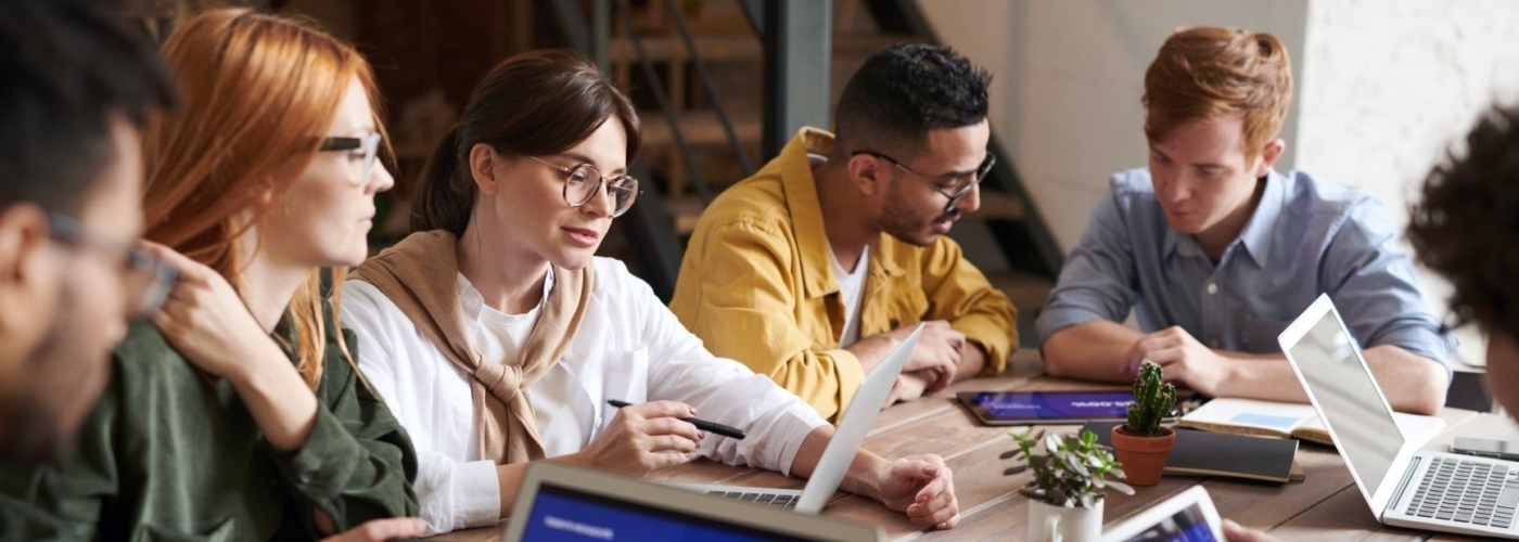Mehrere Personen sitzen an Tisch und arbeiten zusammen