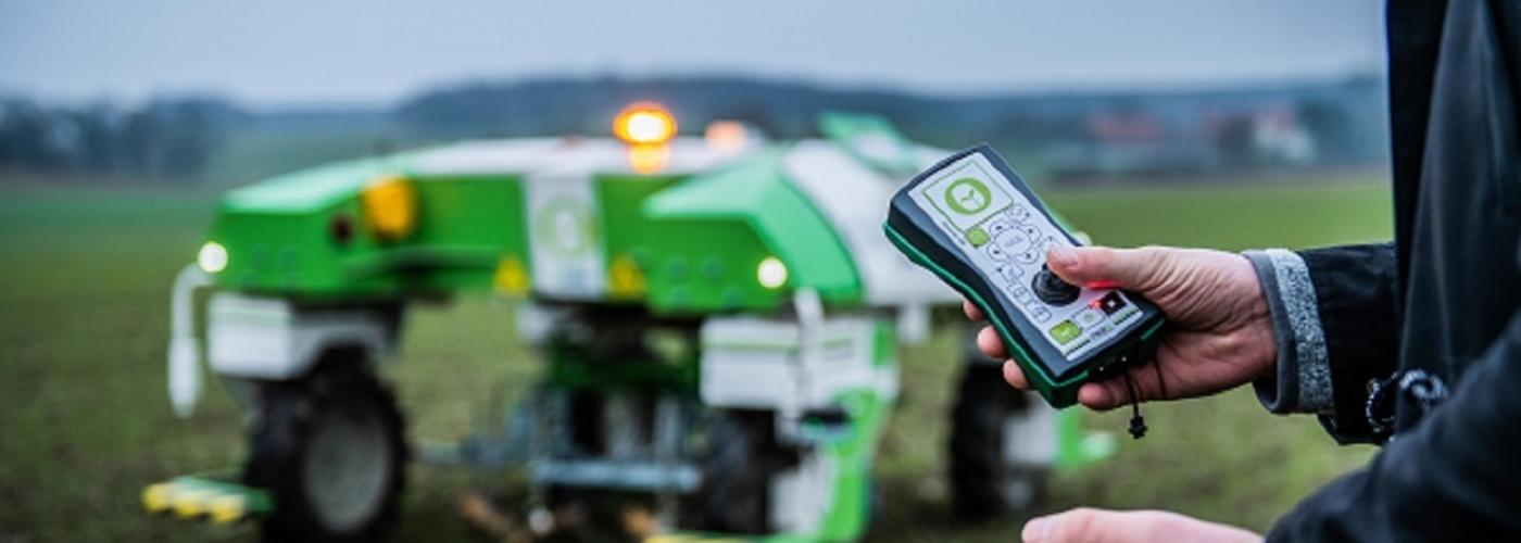 Person steuert landwirtschaftliches Fahrzeug mit einer Fernbedienung