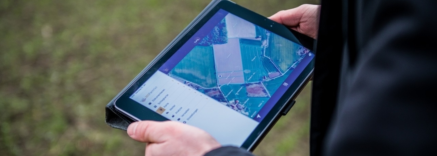 Person hält Laptop mit Drohnenbild eines Feldes