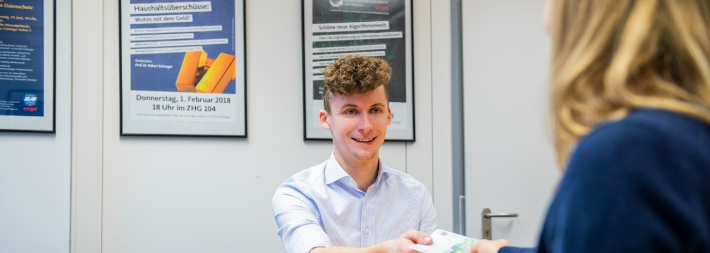 Ein Mann nimmt Geld von einer Frau an, während beide an einem Tisch sitzen.