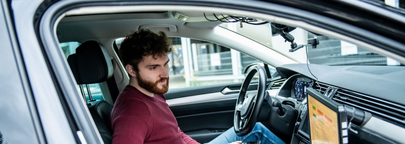 Mann sitzt in einem Auto und schaut auf zweiten Bildschirm