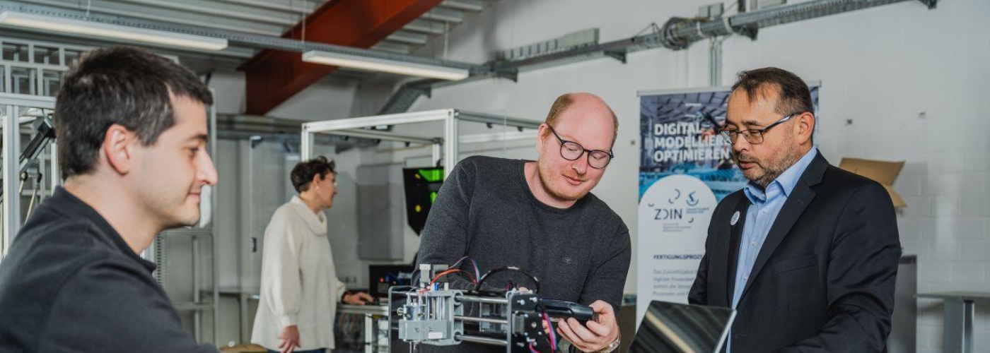 Drei Männer sind in einem Labor und diskutieren über einen technischen Demonstrator.