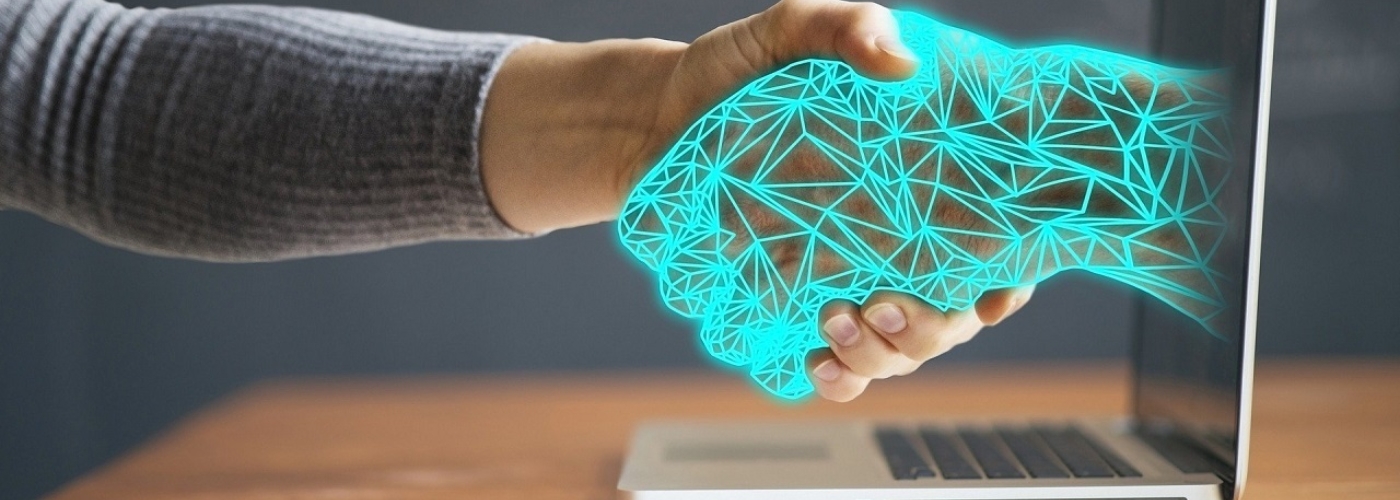 Mann schüttelt Hand mit einem Hologramm, dass aus einem Laptop kommt.