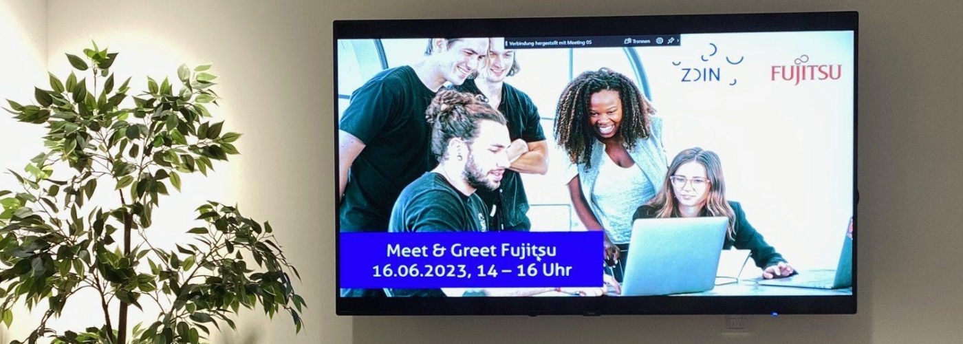 Ein Konferenzraum mit Fernseher auf dem eine Einladung zum Meet & Greet ist