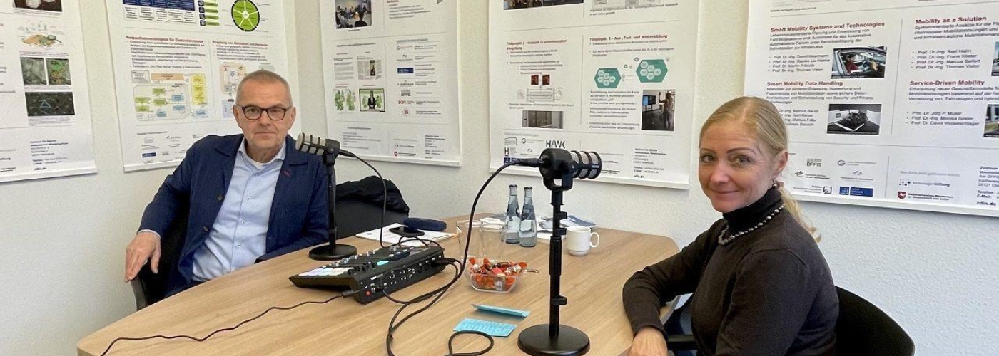 Zwei Personen sitzen an einem tisch vor Mikrofonen