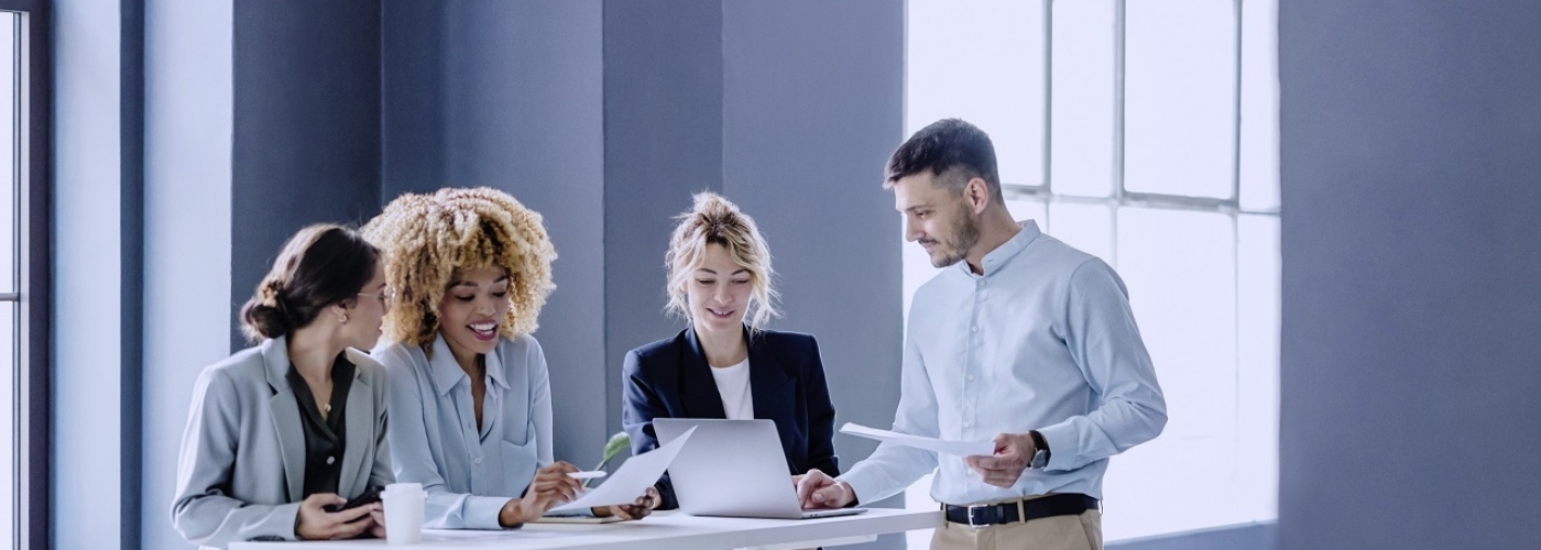 Vier Personen stehen an einem Tisch mit Laptops