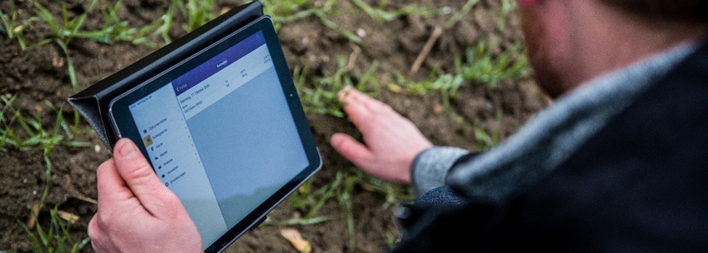 Mann hält Tablet in der Hand und berührt den Boden eines Ackers
