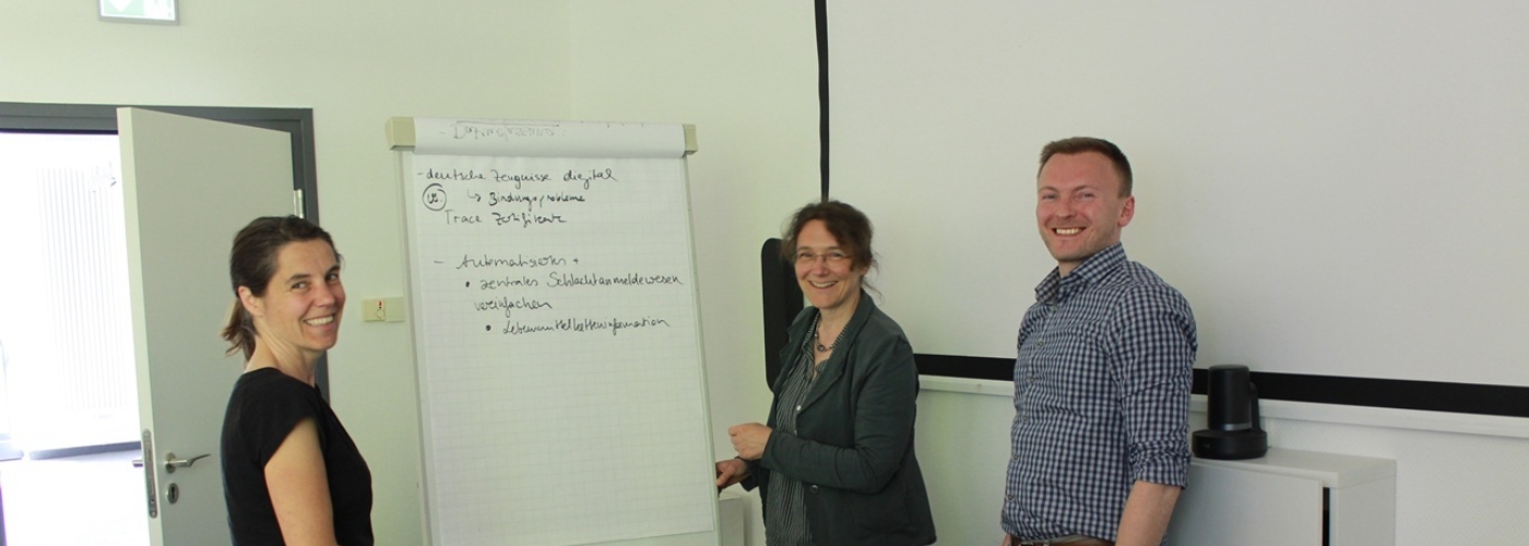 Zwei Frauen und ein Mann stehen vor einem Flipchart in einem Meetingraum.