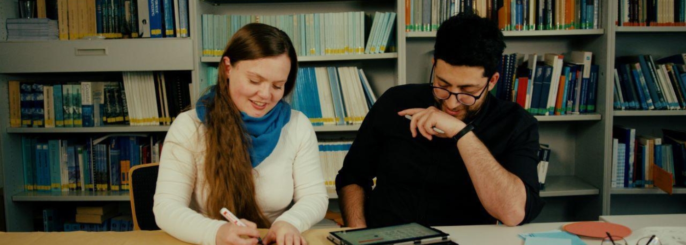 Zwei Personen sitzen an einem Tisch nebeneinander und reden miteinander