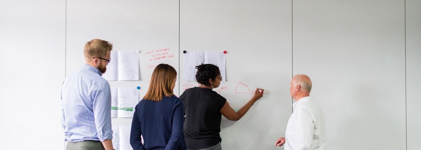 Vier Personen stehen vor einer Wand an der Zettel mit Magneten befestigt sind.