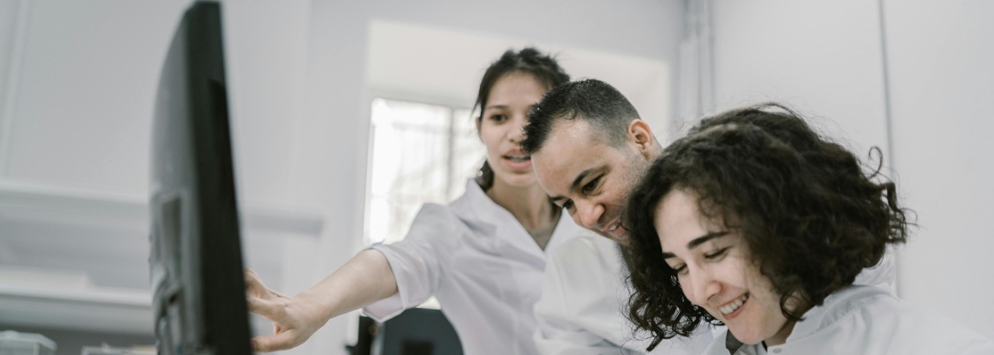 Zwei Frauen und ein Mann in weißen Kitteln arbeiten an einem Computer.