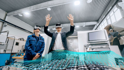 Eine Frau und ein Mann stehen in einer Werkstatt und tragen Virtual-Reality-Brillen.