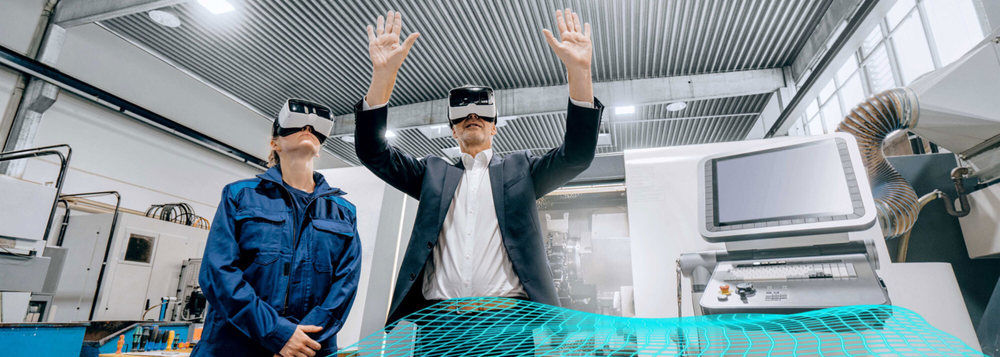 Eine Frau und ein Mann stehen in einer Werkstatt und tragen Virtual-Reality-Brillen.