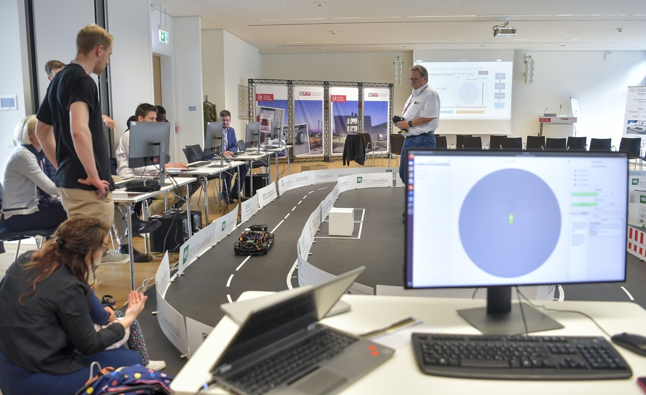 Ein Modellauto fährt durch einen Parcour, Menschen stehen darum und schauen zu.